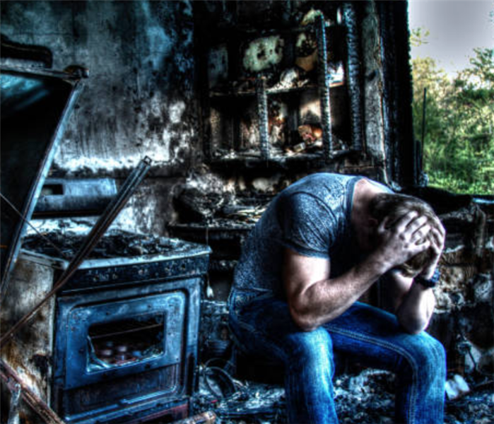 A fire damaged kitchen with a man sitting with his head in his hands