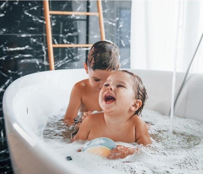 Two toddlers playing in full bathtub